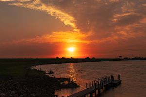 Warm sunset colors reflect off calm waters with a wooden dock silhouetted against the horizon.