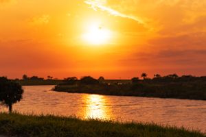 Spectacular orange sunset over a coastal waterway with silhouetted vegetation and reflective waters.