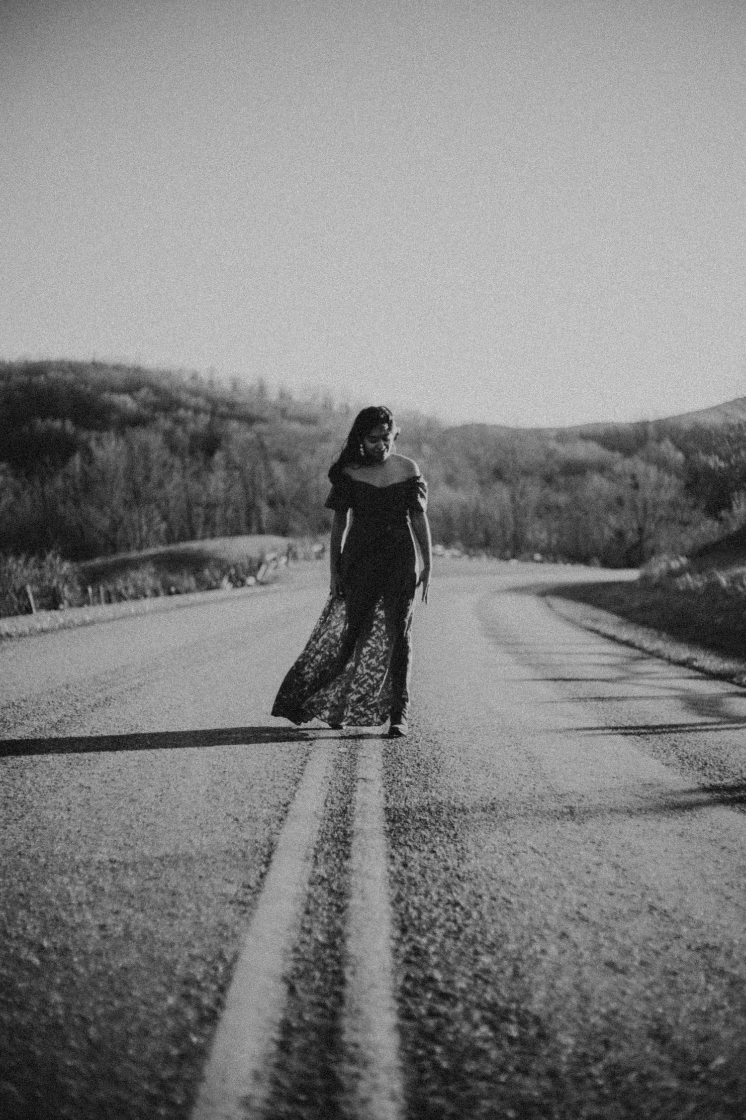 Black and white portrait of woman standing on center line of empty rural road.