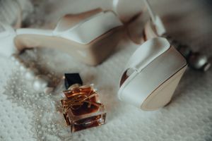White bridal heels and a perfume bottle arranged on a textured white surface.