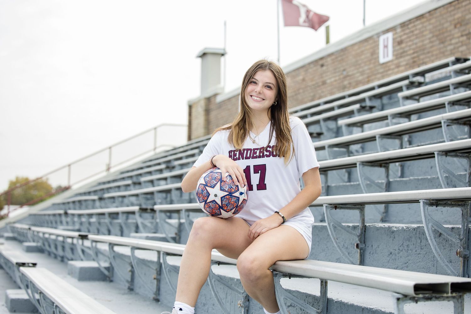 Soccer player poses with ball on stadium bleachers wearing team jersey number 17.
