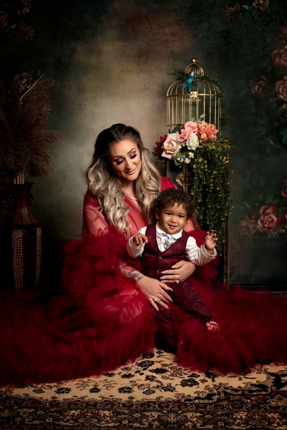 A dramatic portrait in a vintage setting with red dress, floral decor, and ornate birdcage.