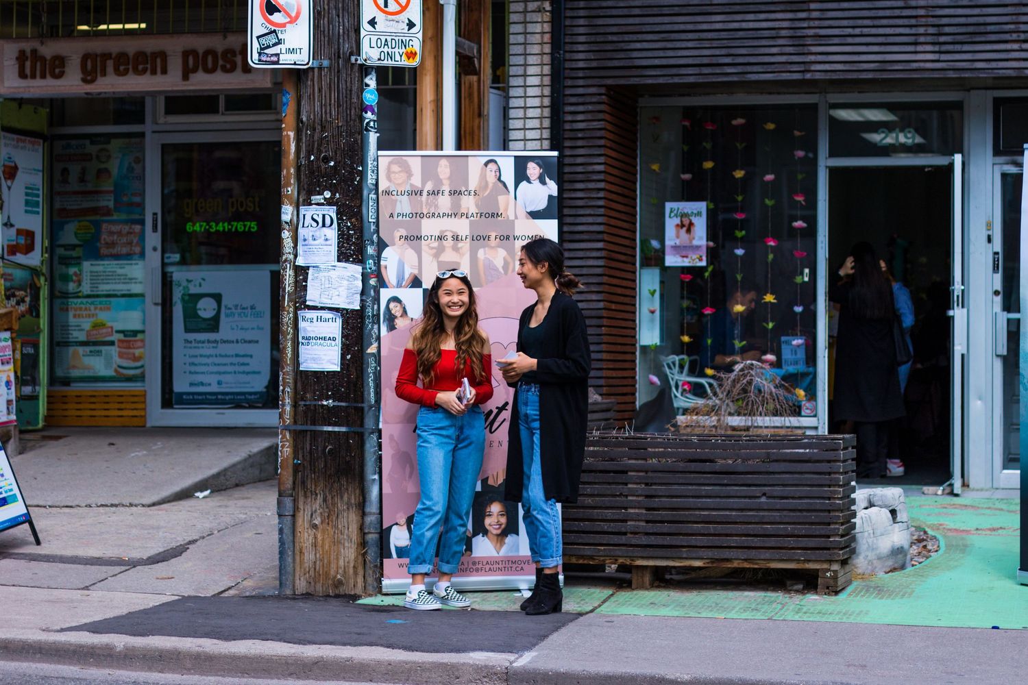two women of color in front of a flaunt it standing banner at the side of the street