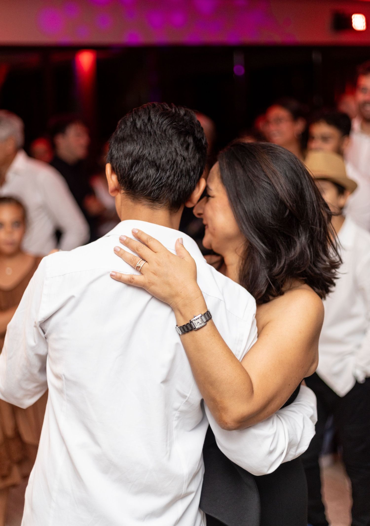 A couple in white sharing an intimate dance moment under pink lighting at an event.