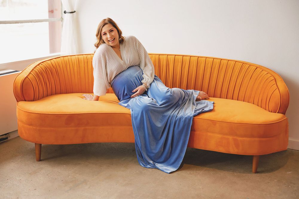 Relaxed maternity pose on orange velvet couch with blue fabric draping.