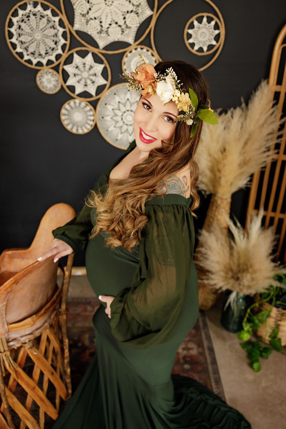 A maternity portrait featuring flowing dark green dress and floral crown against a backdrop of decorative snowflakes.