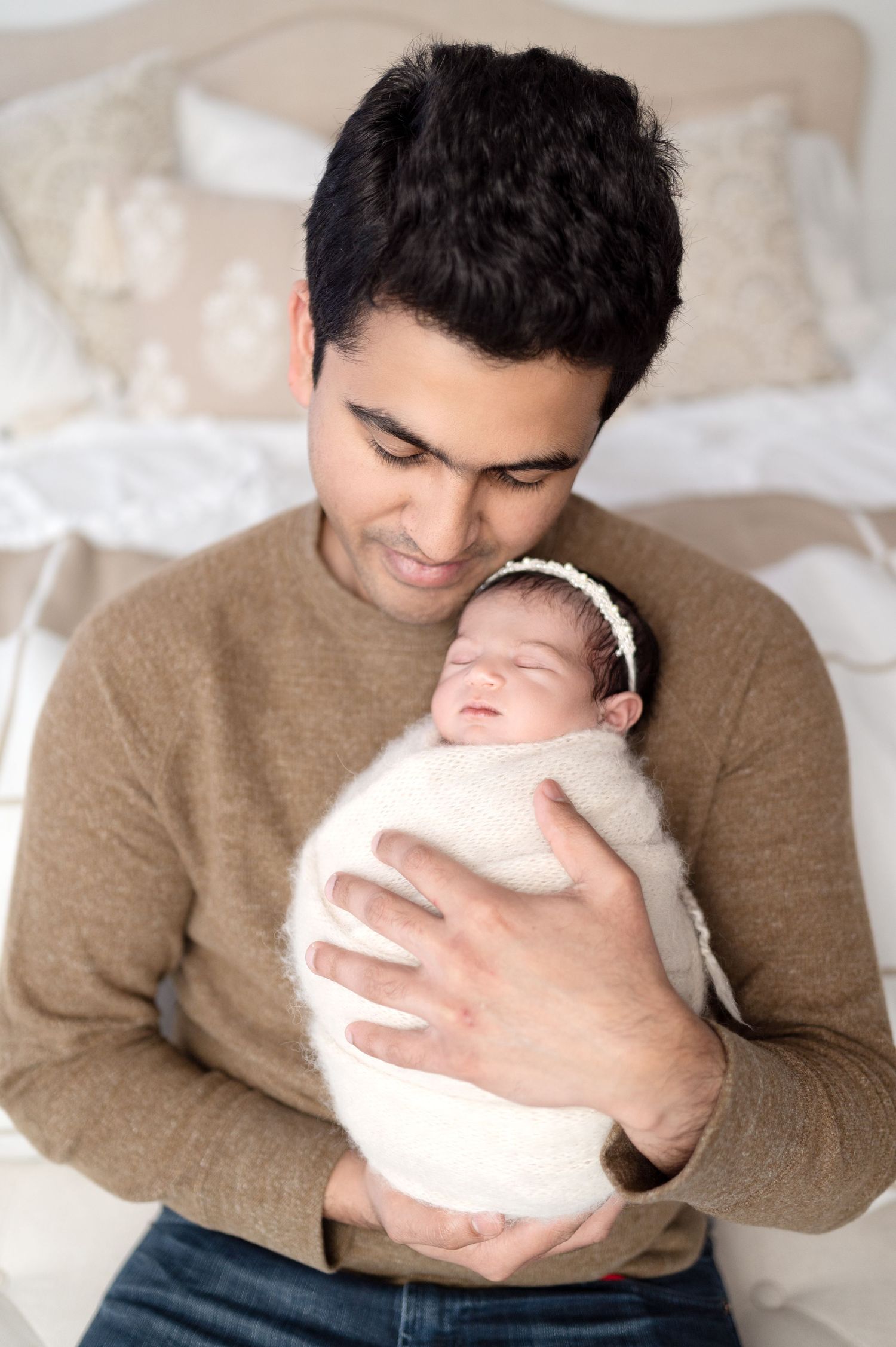 Tender moment of person in tan sweater holding and admiring a sleeping newborn.