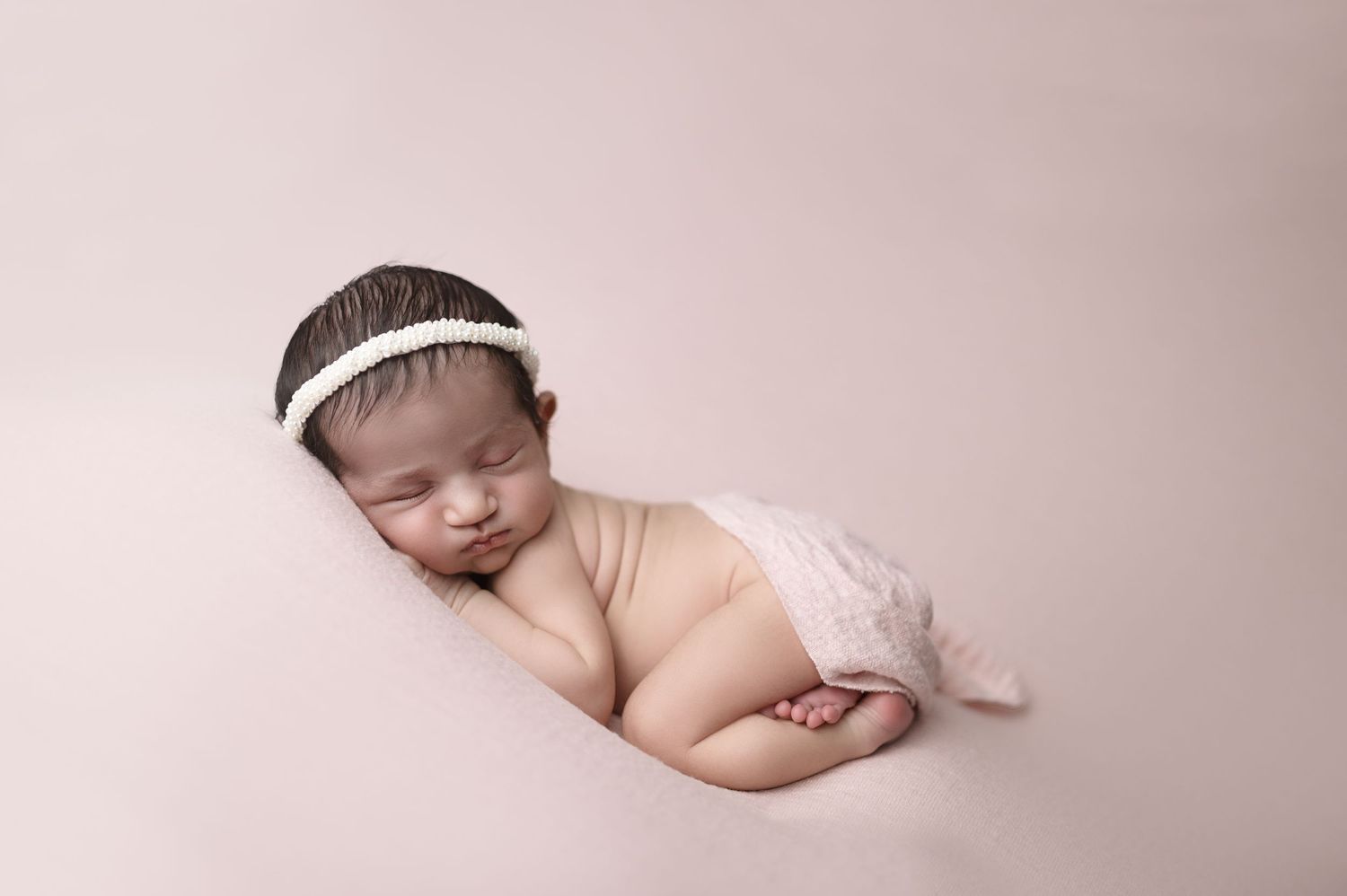 Side view of sleeping newborn with white headband in minimalist setting.