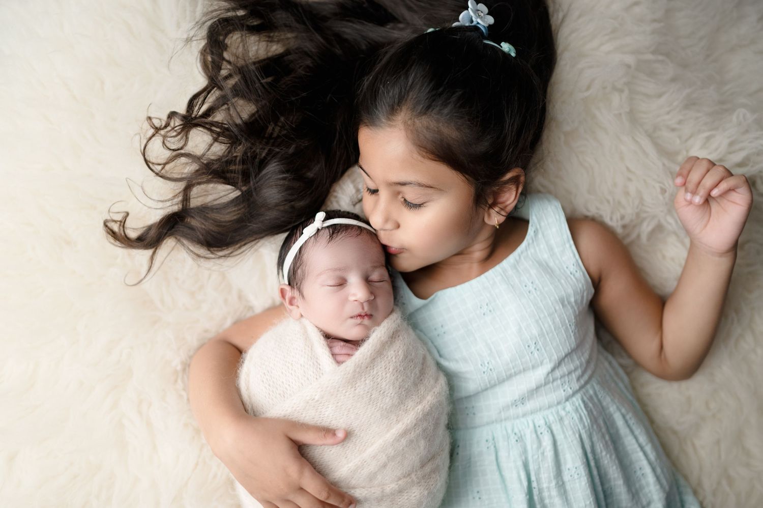 Tender sibling photography session with sister and newborn on plush white background.