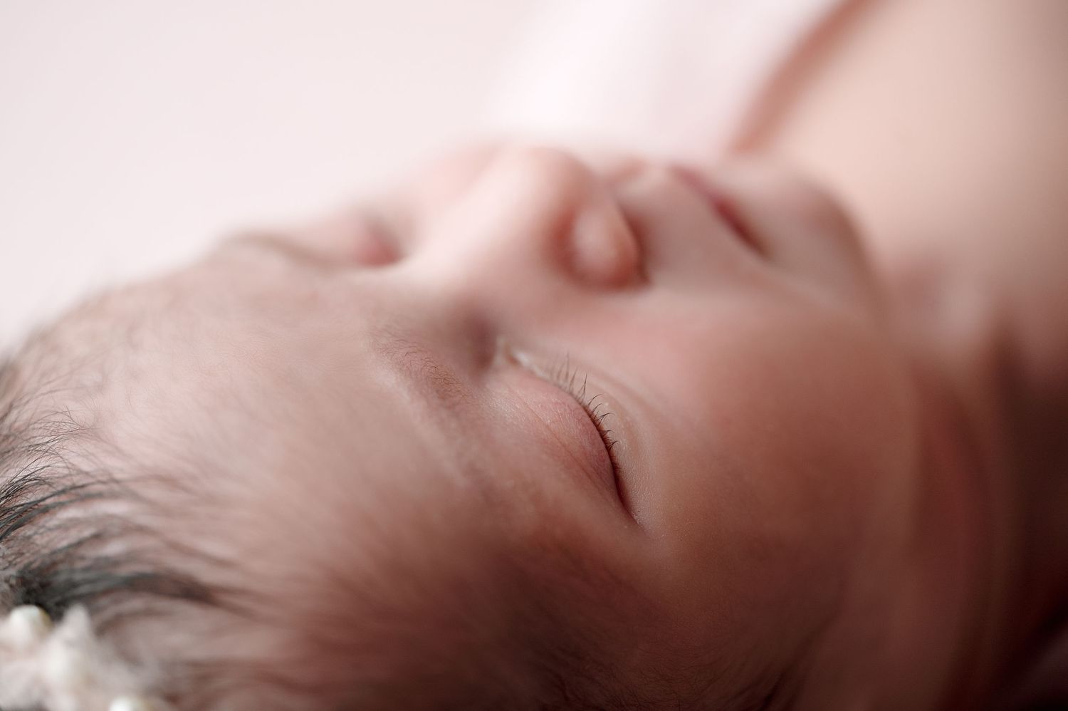 Serene portrait of sleeping newborn with soft focus and pink tones.