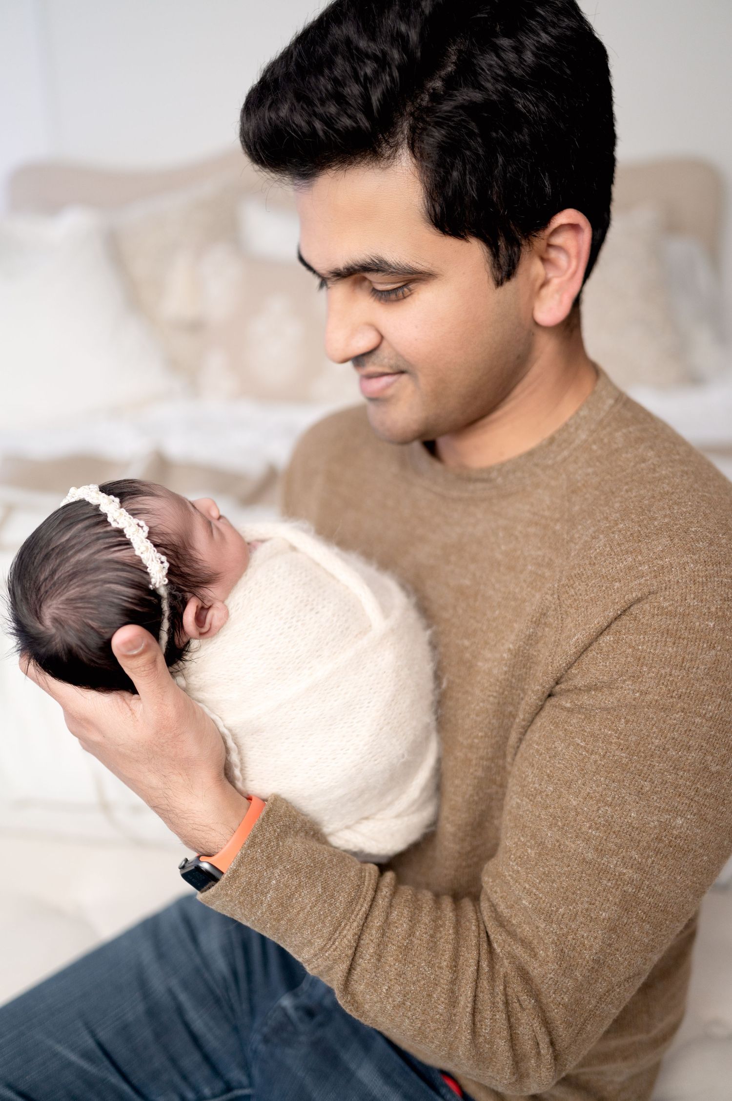 Person in brown sweater gently cradling a newborn baby in soft, gentle lighting.