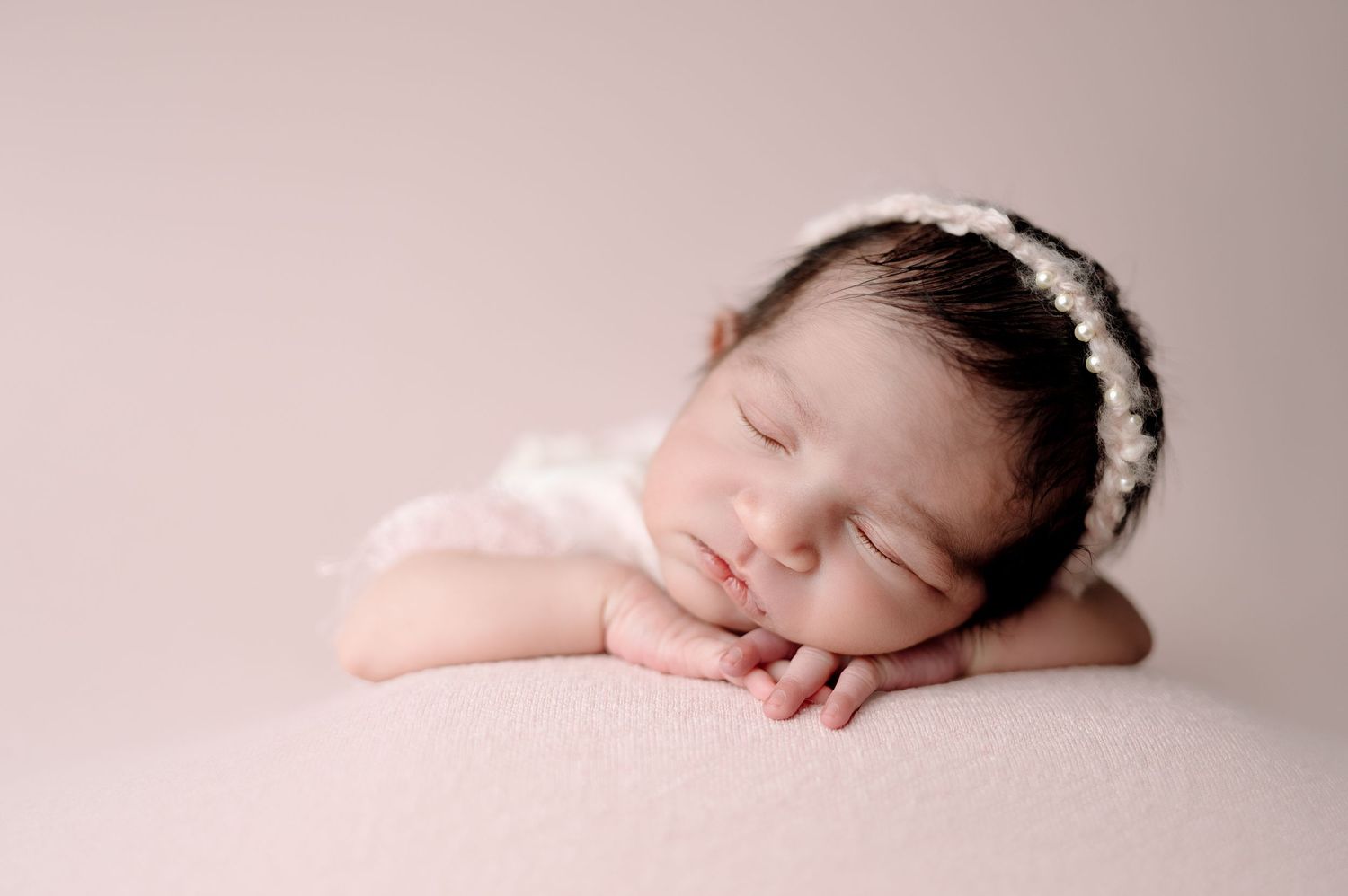 Artistic profile view of sleeping newborn against neutral pink background.