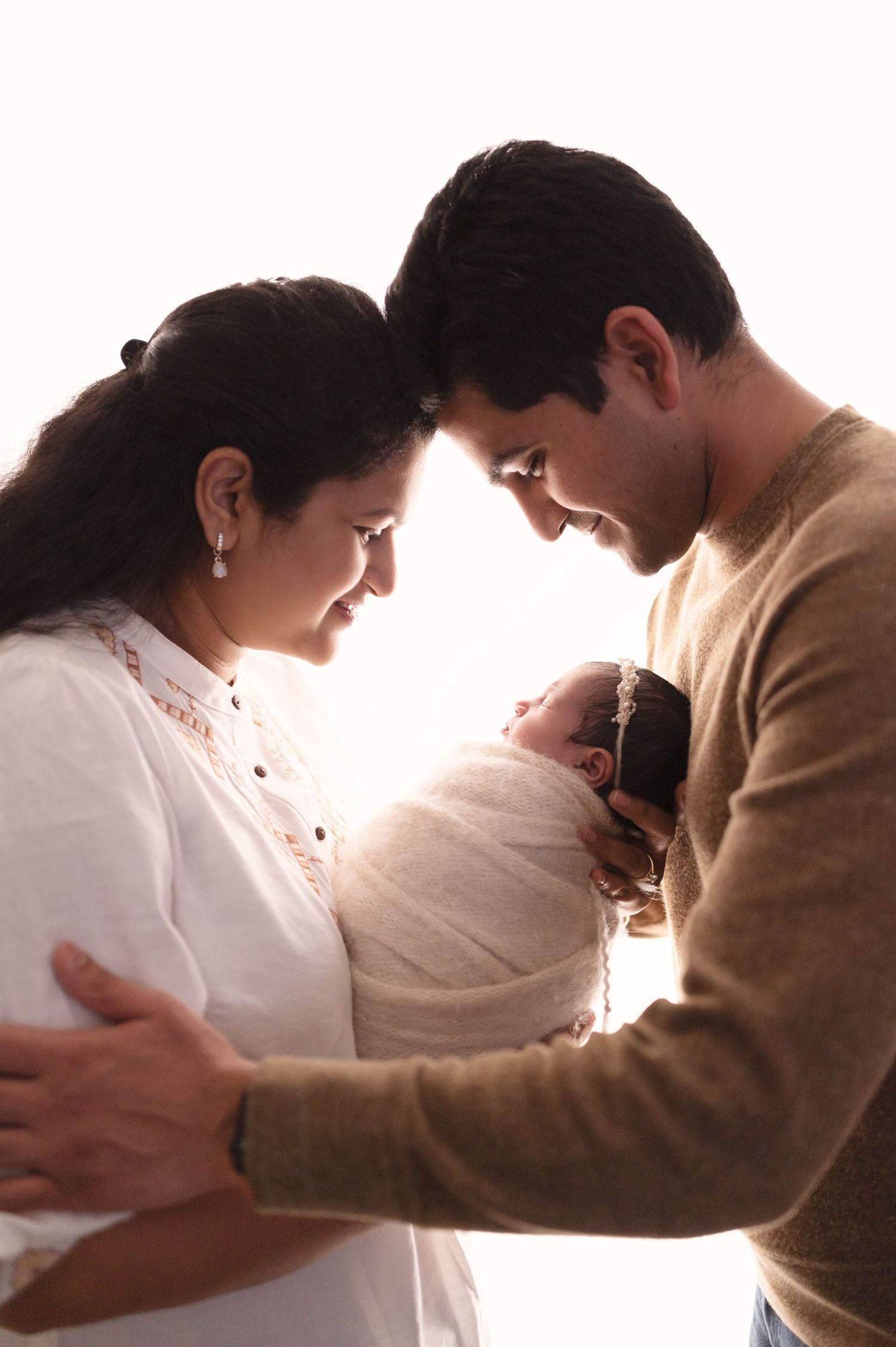 Artistic silhouettes capture tender moments between parents and their newborn baby against bright background.