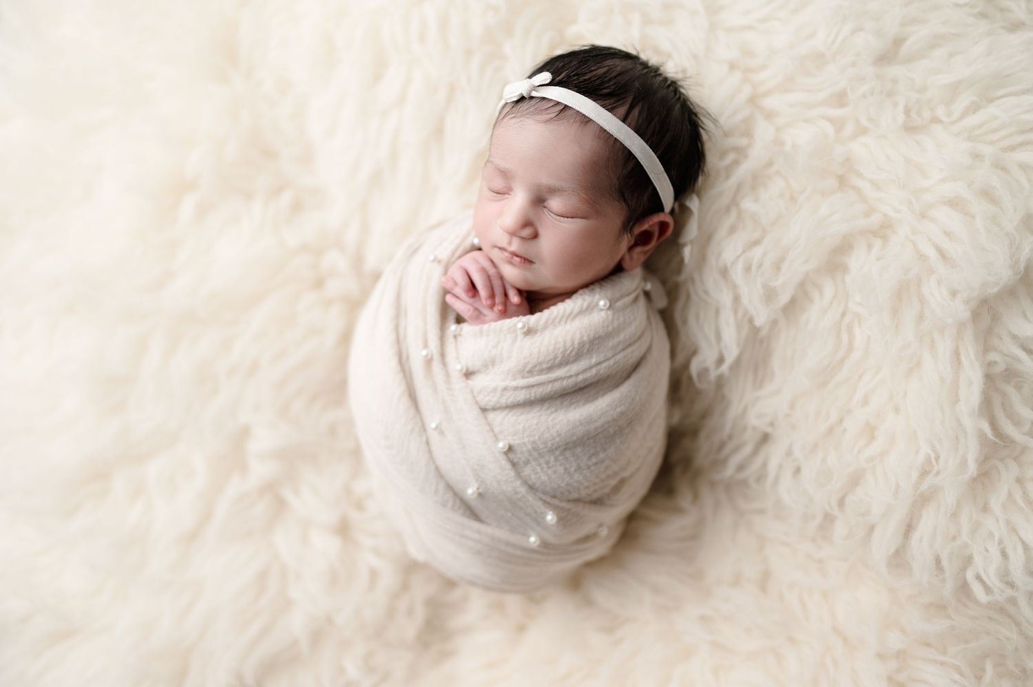 Professional newborn portrait session with baby sleeping soundly on white fur rug.