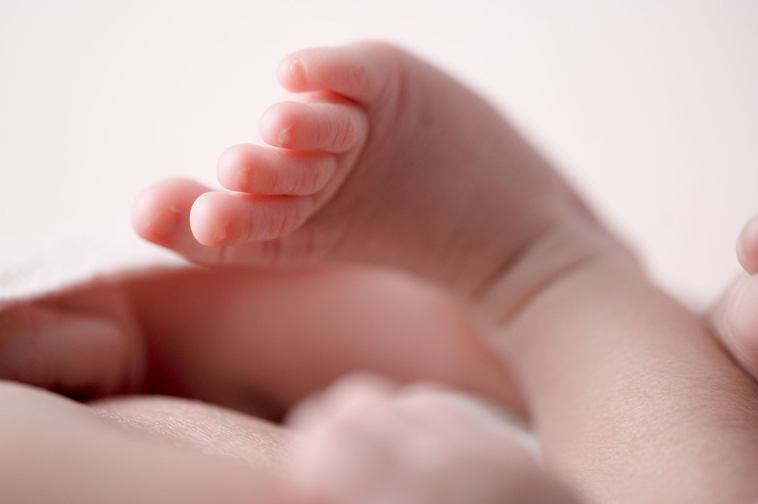 Close-up detail of newborn baby's tiny hands in dreamy pink lighting.