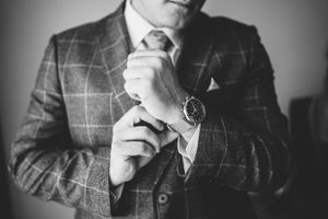 Close-up of hands adjusting a watch while wearing a plaid suit jacket in black and white.
