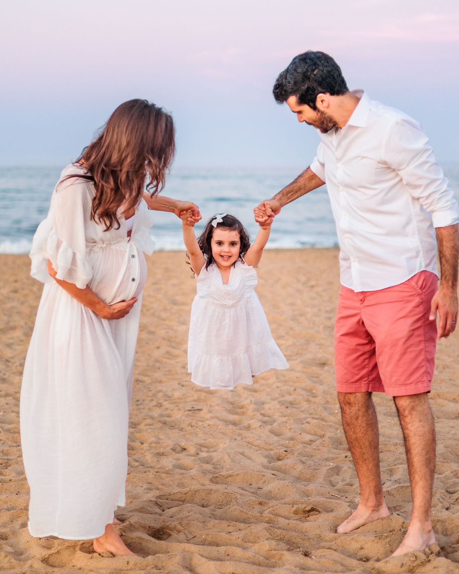 A joyful family moment on the beach at sunset with parents and young child playing.