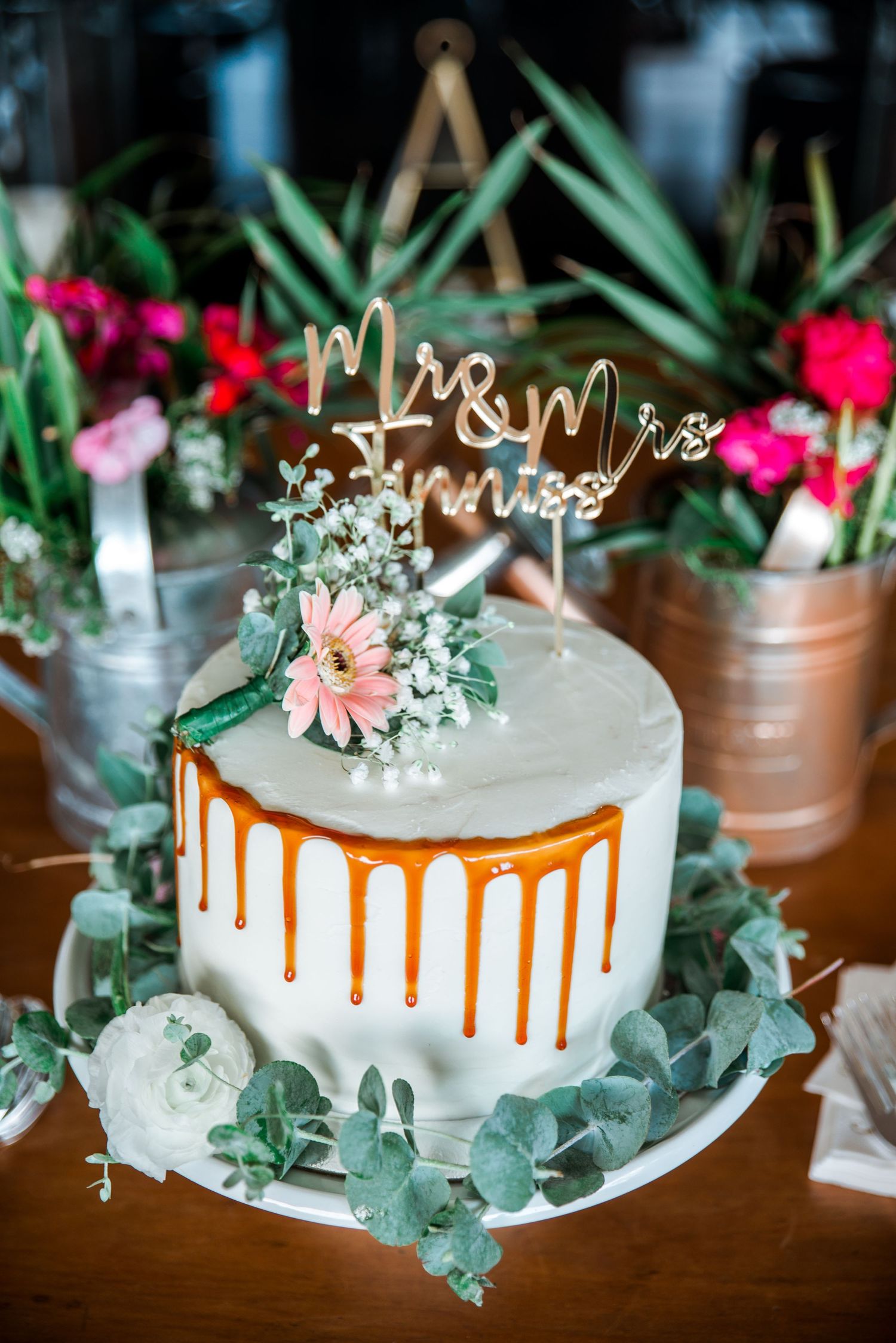Elegant white wedding cake with gold drip, floral decorations and 'Mr & Mrs' topper.