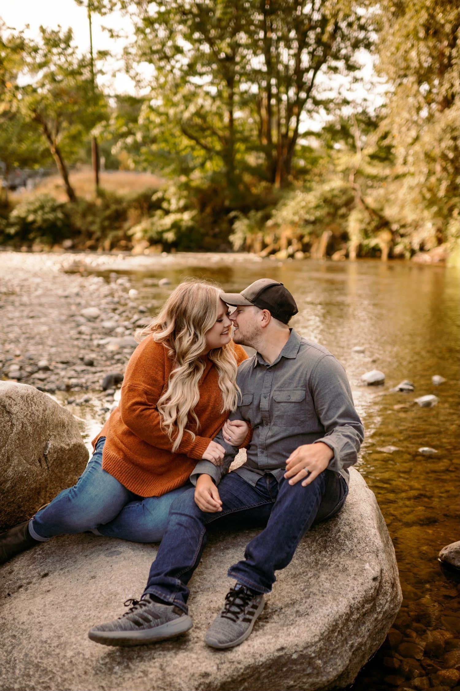 Couple relaxing together on large rocks by a peaceful river during autumn.