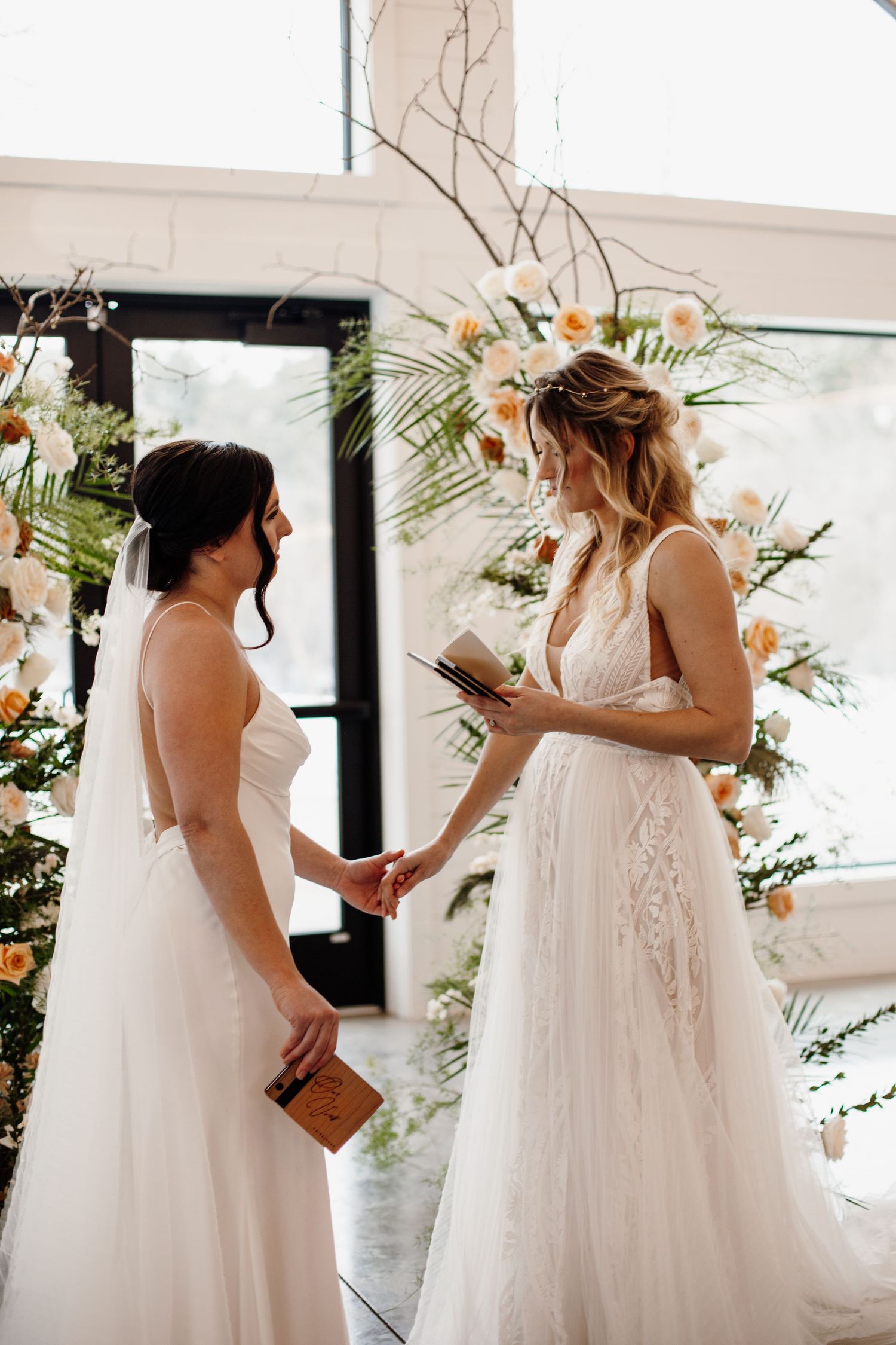 Two brides in white wedding dresses share a moment during their ceremony.