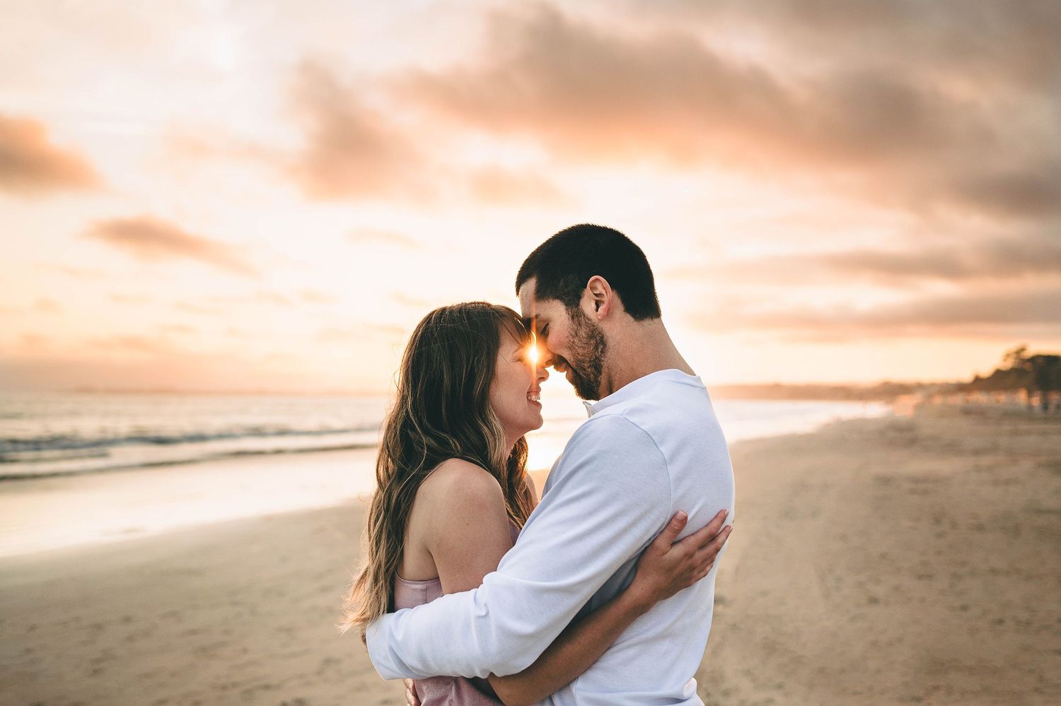 Intimate beach portrait of a couple embracing during sunset with golden clouds in the sky.