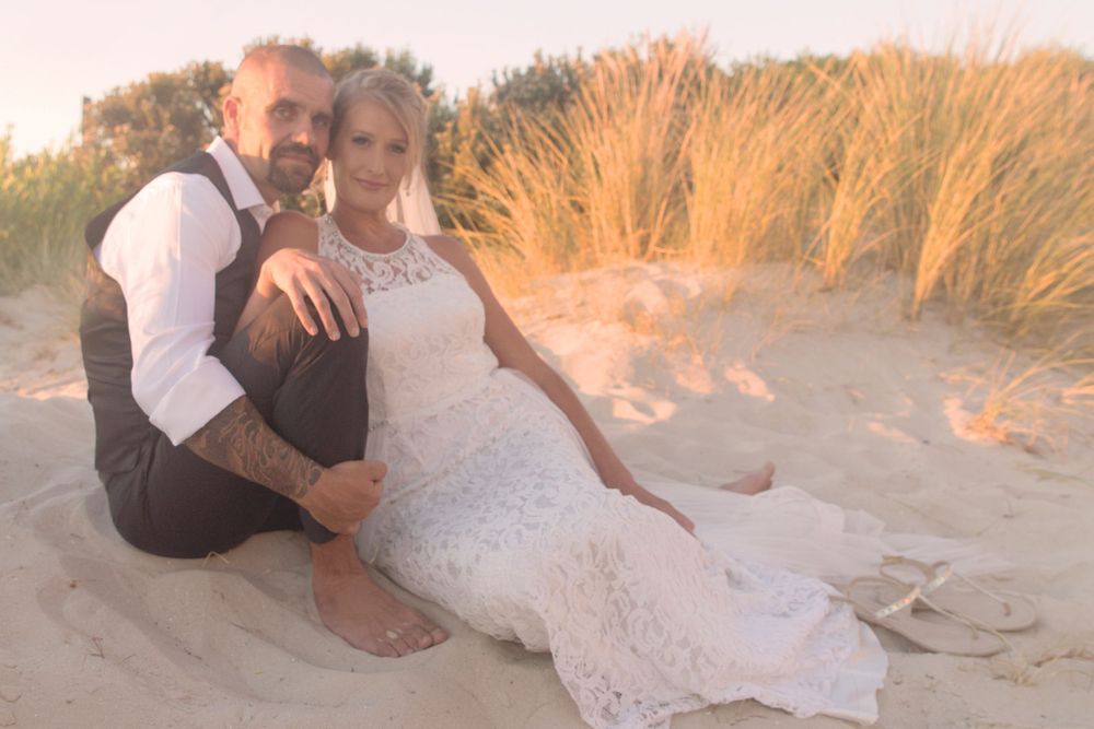 A couple shares romantic moments on sandy beach dunes during golden hour wedding photos.