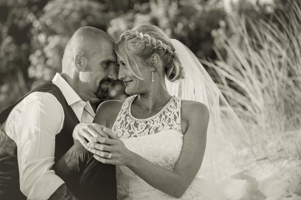 Black and white wedding portraits capture intimate moments between newlyweds on a beach.
