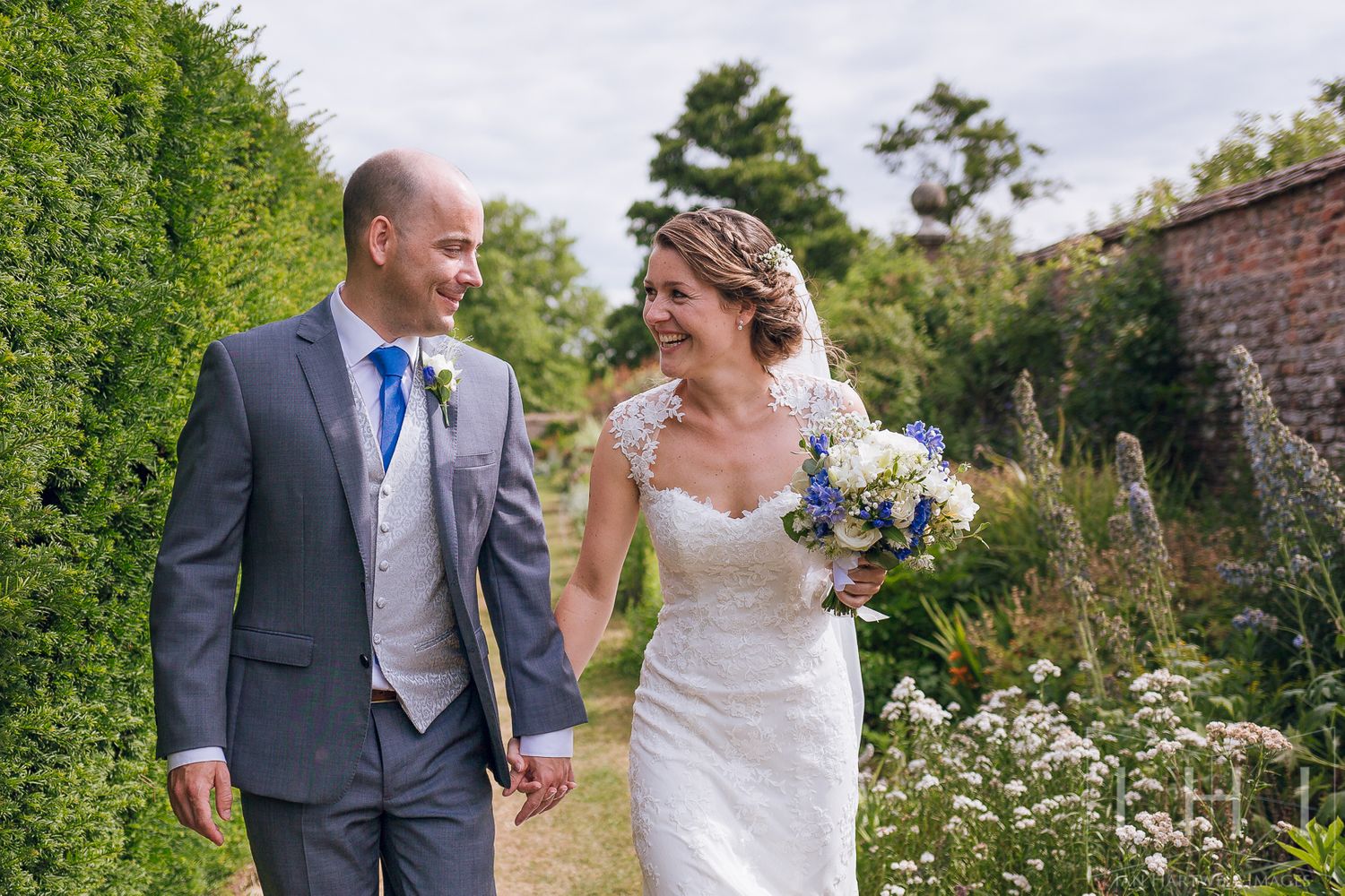 A bride and groom hold hands while walking in the grounds of Birtsmorton Court. Looking at each. smiling and laughing.