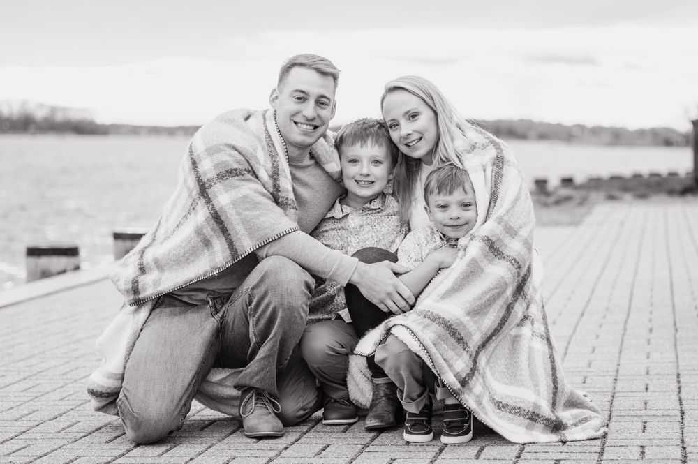 A family of four wrapped in a blanket sits together on a wooden deck by the water in Annapolis.