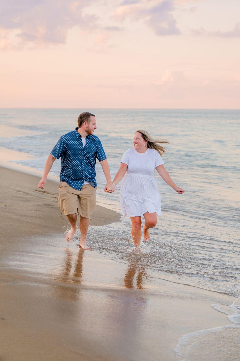 A newlywed couple runs hand in hand along a beach at sunset.