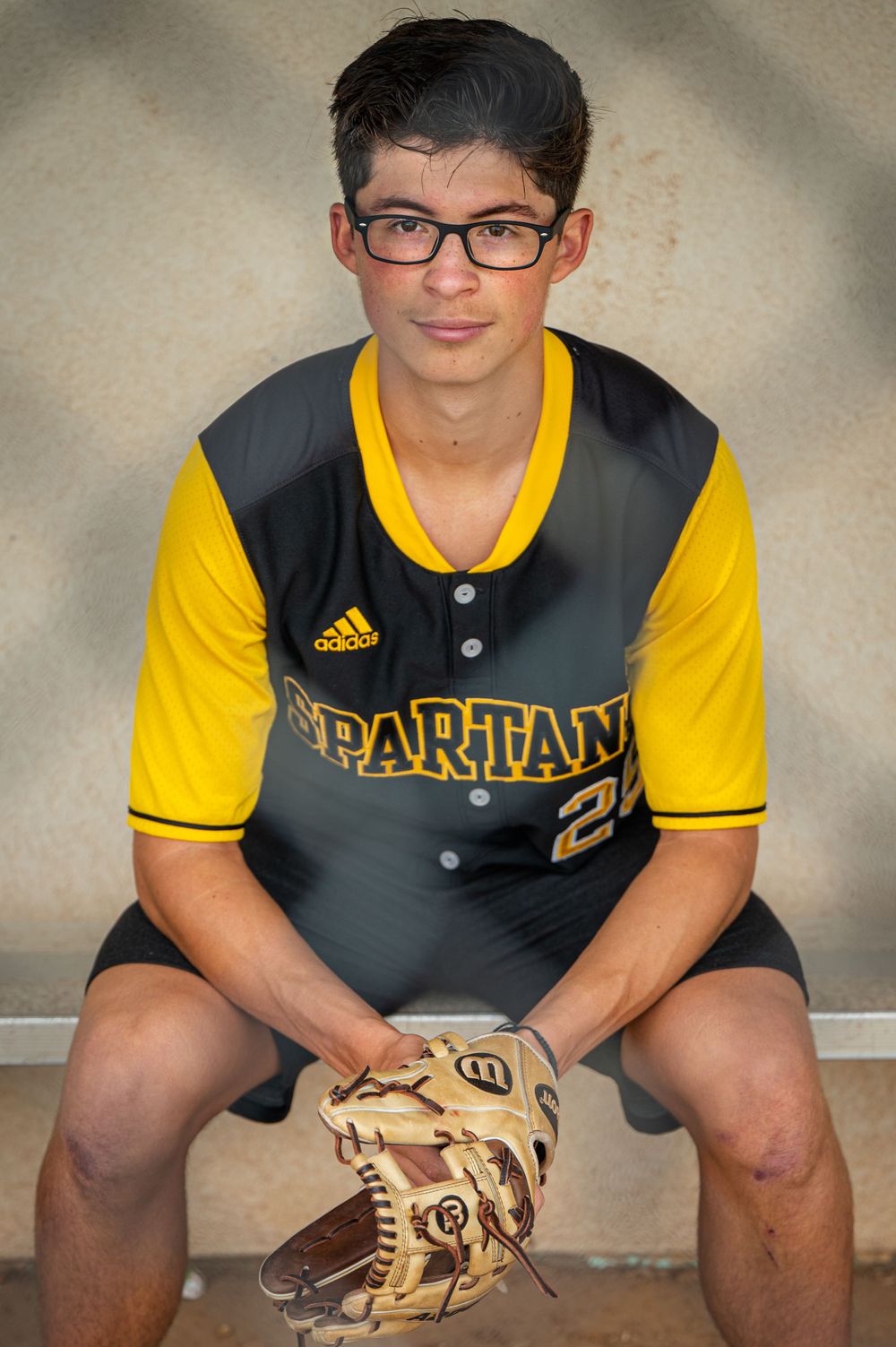 A senior baseball player in a black and yellow Spartans uniform poses with their glove.