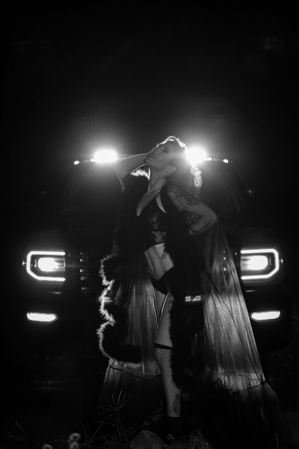 Silhouettes of figures illuminated by car headlights in a dark nighttime scene.
