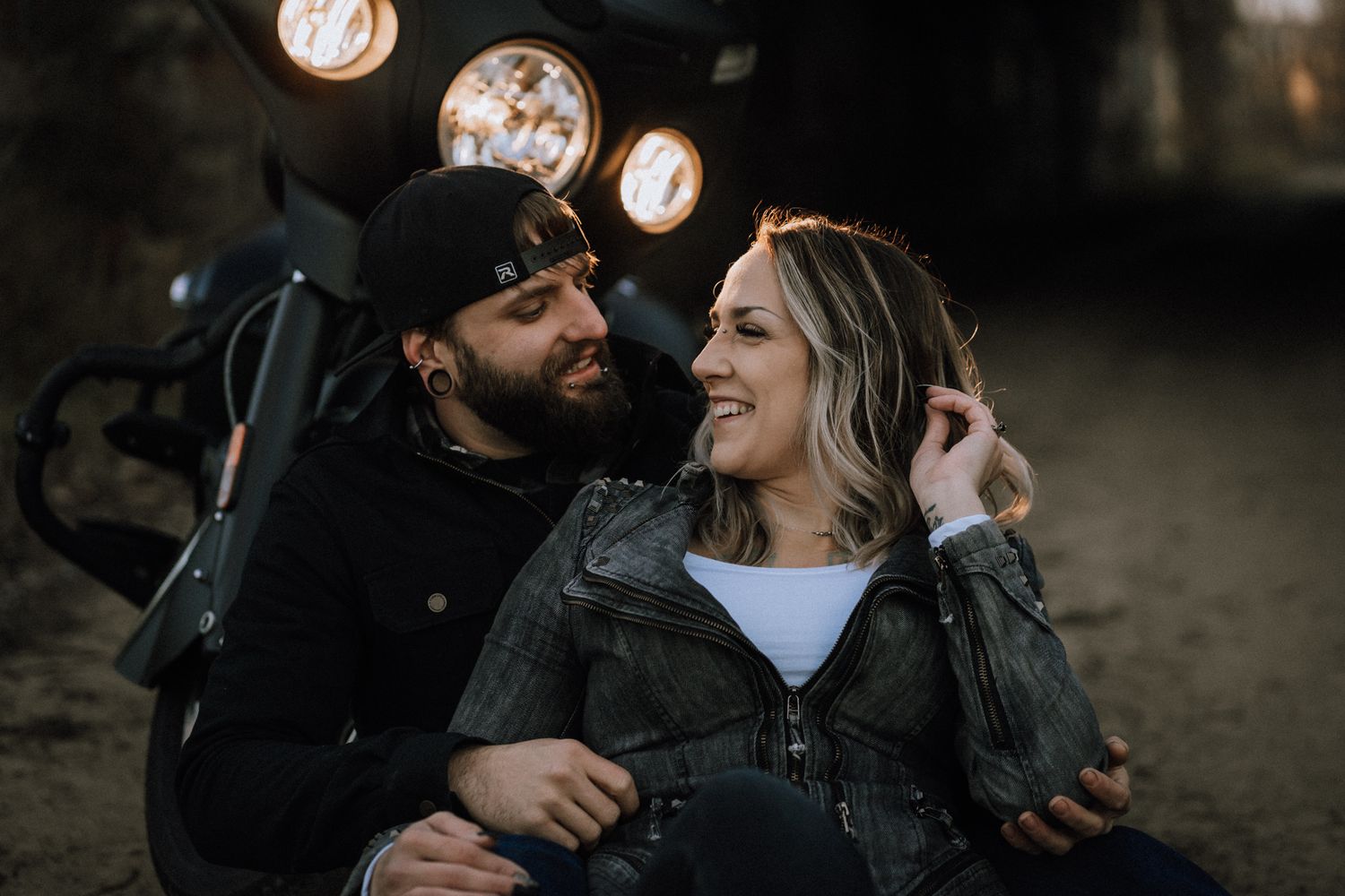Intimate outdoor portrait with bokeh lights showing a laughing couple in dark clothing sharing a tender moment.