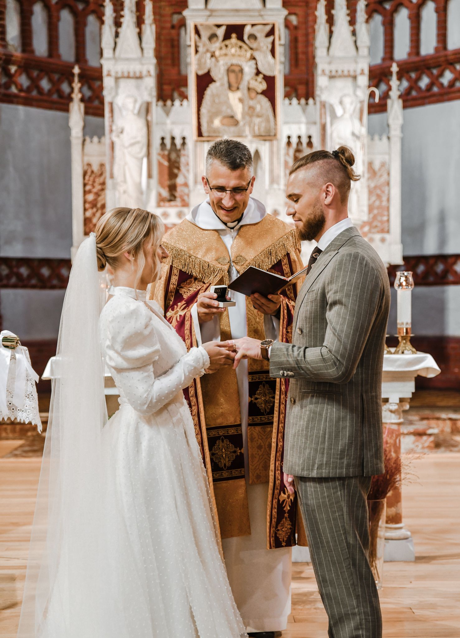 Couple exchanges vows during wedding ceremony in ornate cathedral setting.