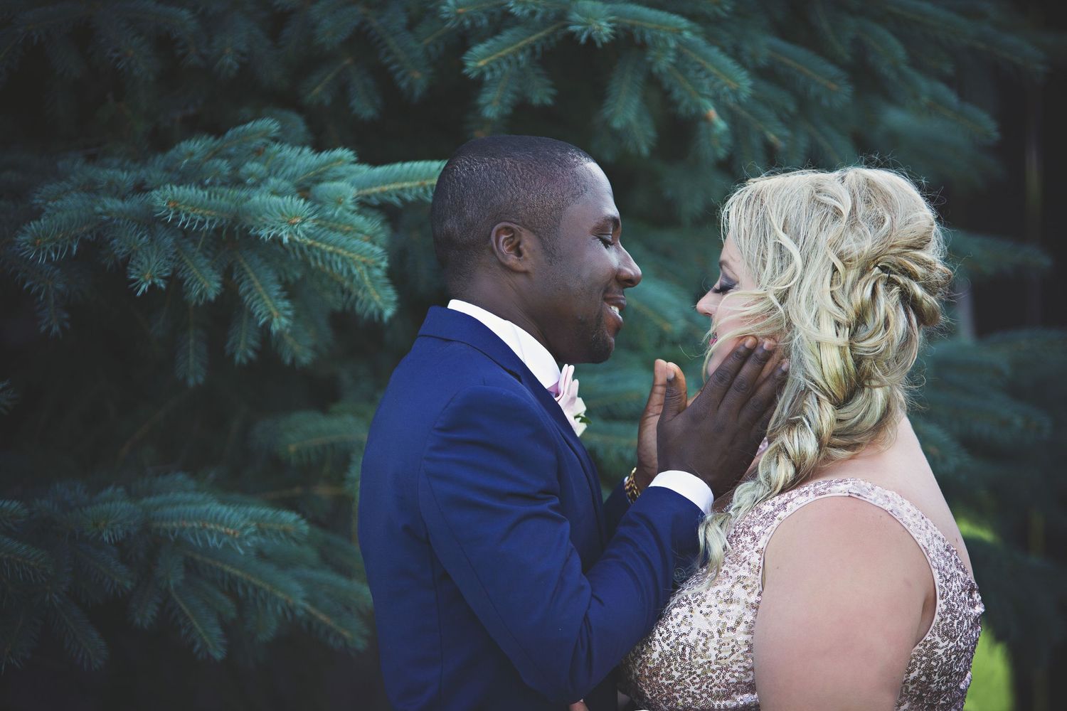 Romantic wedding moment captured against evergreen trees in soft lighting.