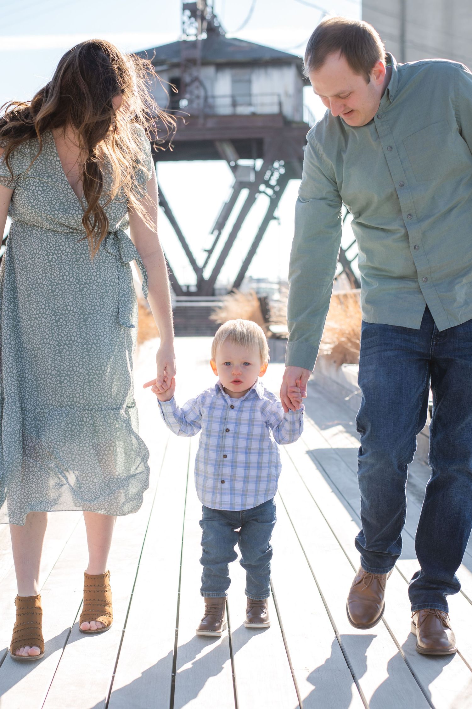 Family walking together on wooden deck with industrial structure in background.