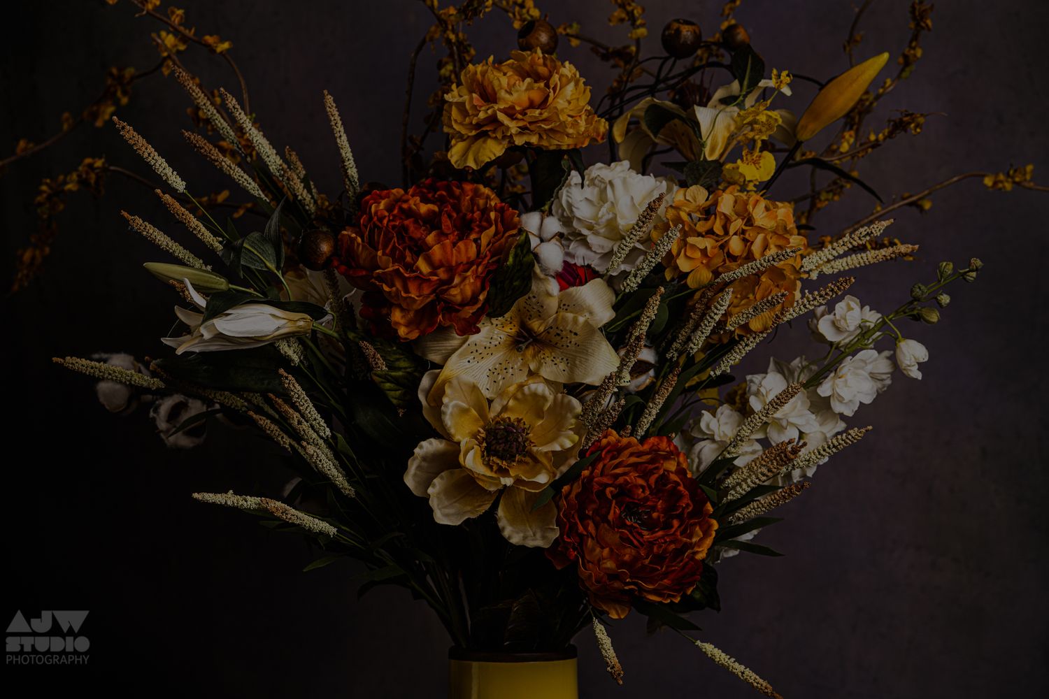 Dark and moody floral arrangement with orange and red blooms in a yellow vase.