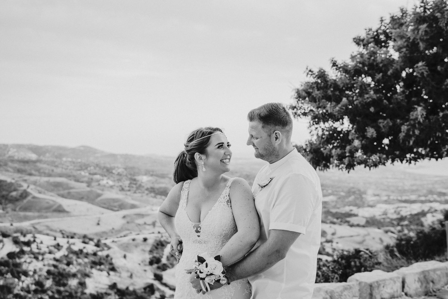 A candid black and white portrait of a couple against a scenic hillside backdrop.