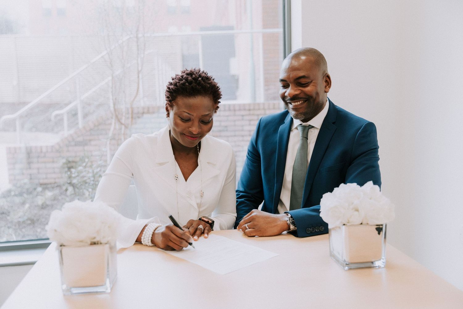 A couple reviews and signs paperwork together at a bright office table.