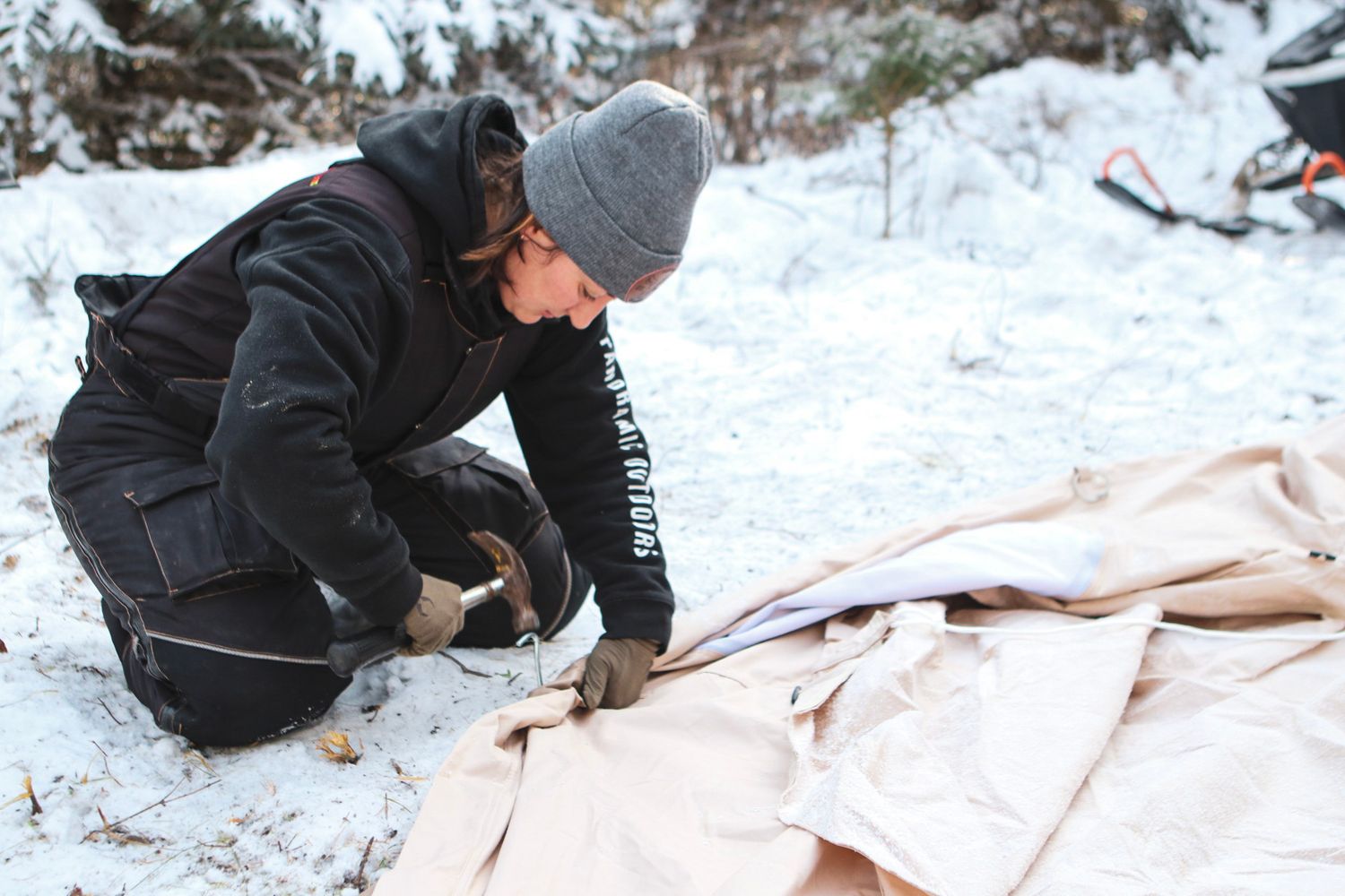 Setting up winter camping equipment on protective ground cover in snow.