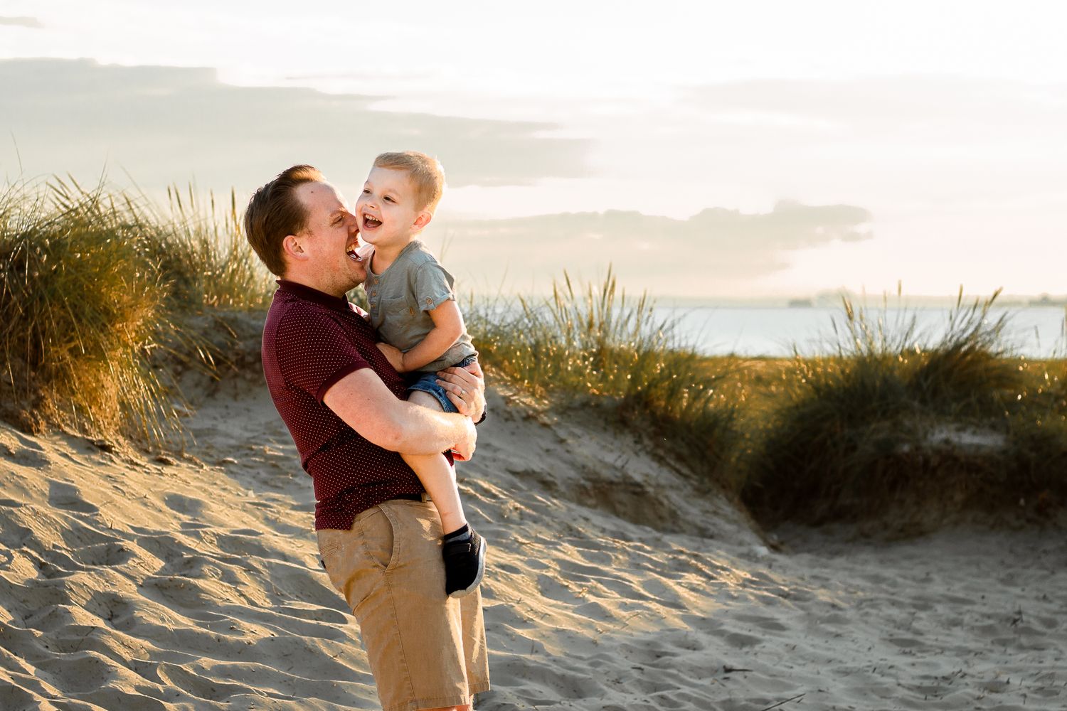 On a beach on Hayling Island a Father stands holding his three year old Son they are laughing in the sun.