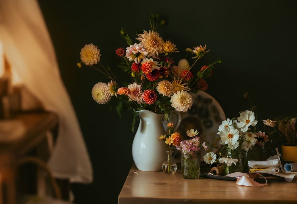 Mixed flower arrangement in white vase with dahlias and wildflowers on wooden table.