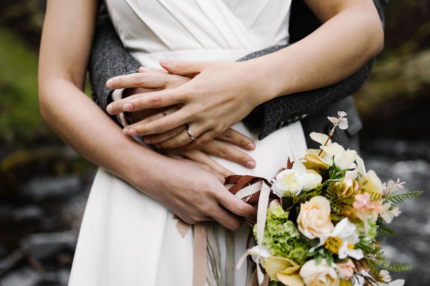 Elegant wedding bouquet with white roses and greenery held against a white dress.