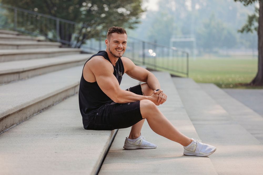 Athlete in black workout clothes sitting on concrete steps outdoors.