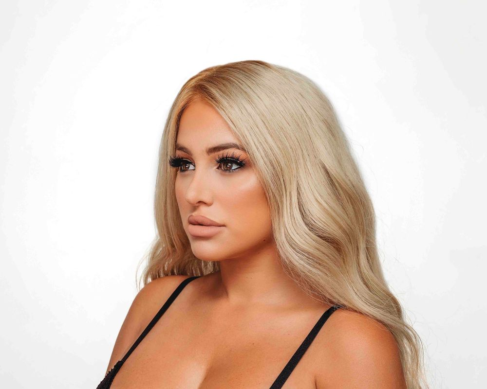 Professional beauty portrait of a woman with long wavy blonde hair against white background.