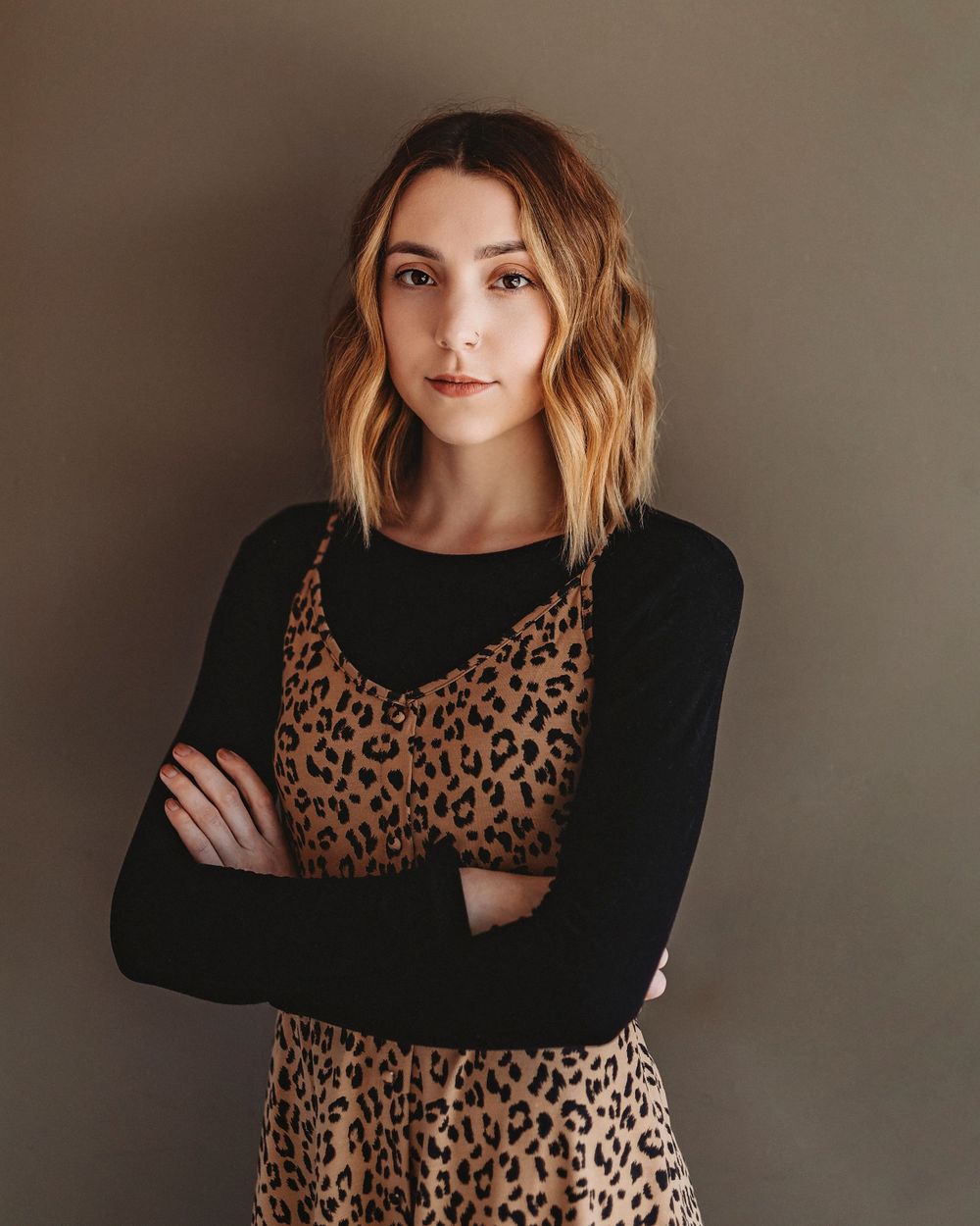 Stylish woman wearing leopard print dress and black long sleeve top against neutral background.