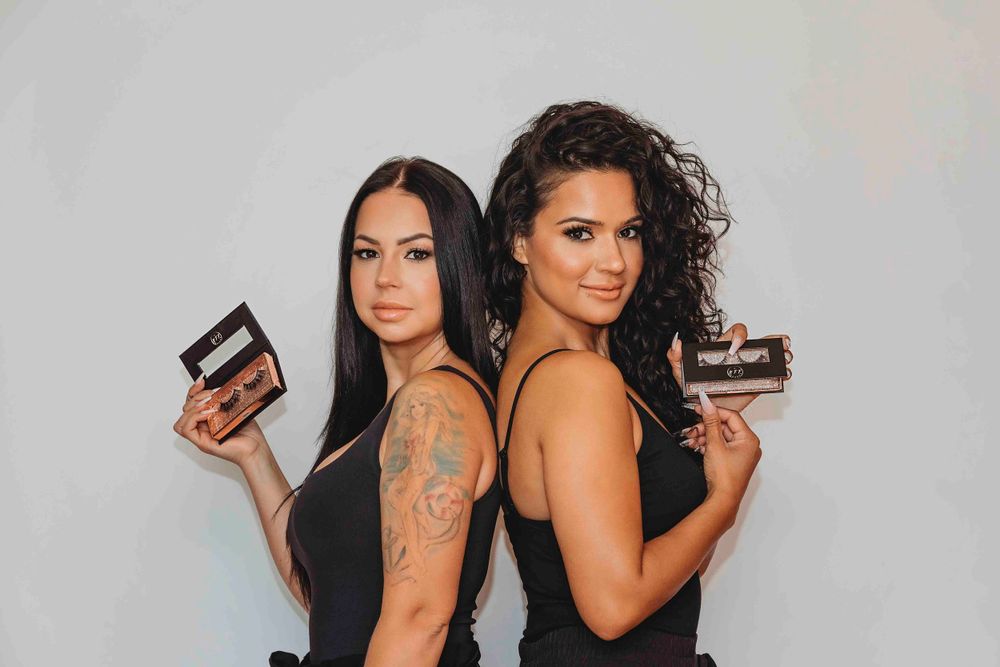 Two women in black outfits pose back-to-back holding chocolate desserts.
