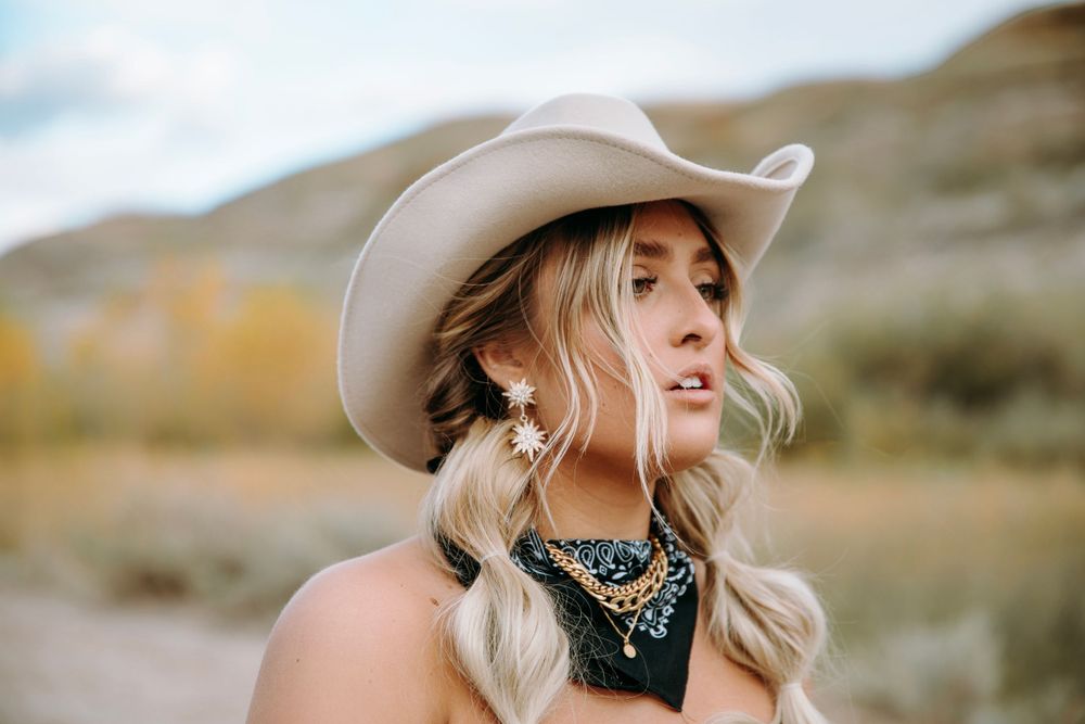 Woman in cowboy hat and bandana looking away in desert landscape.
