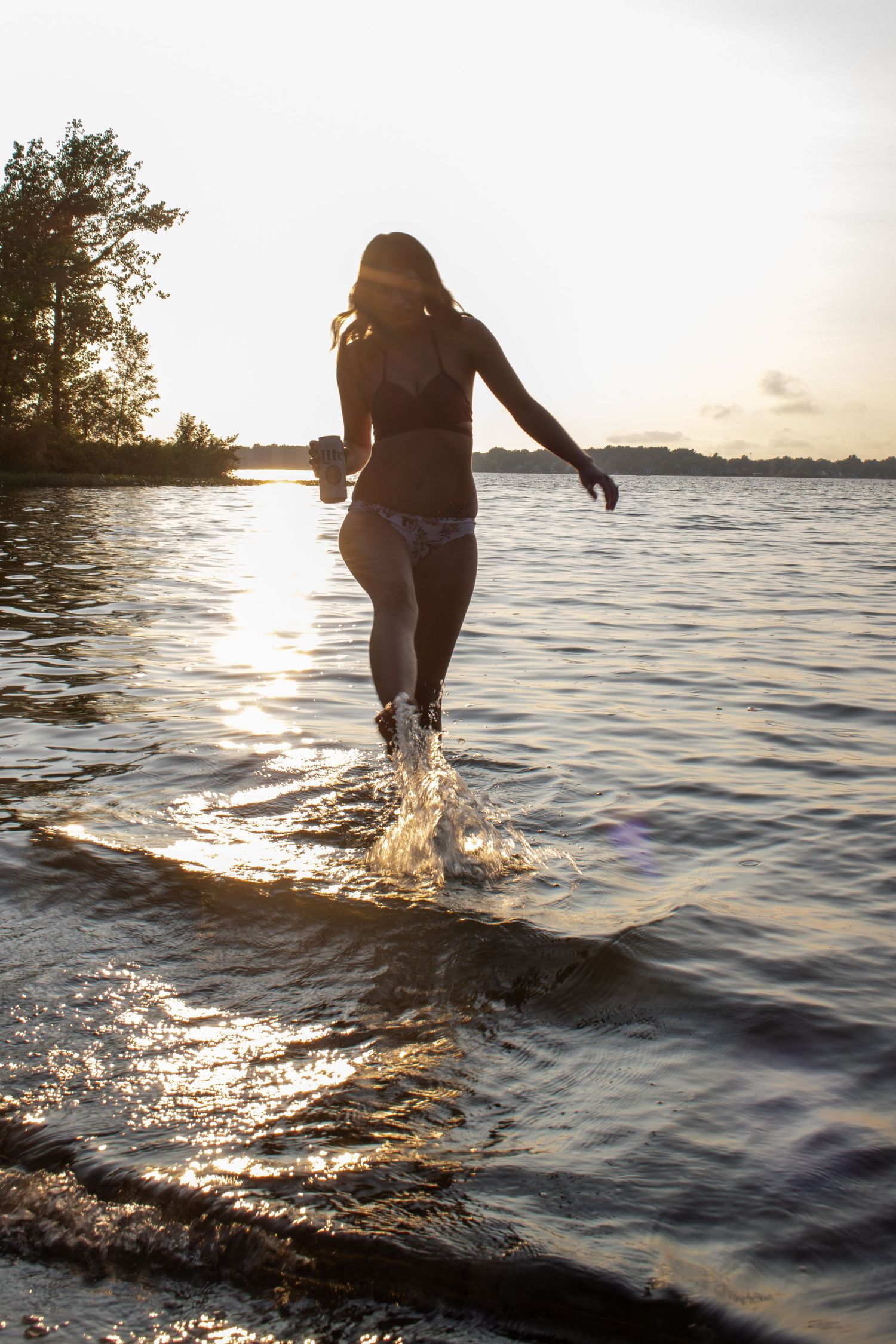 Silhouette splashing through water at sunset with trees in background.