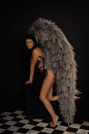 Artistic boudoir photo with model and dramatic angel wings on checkered floor.